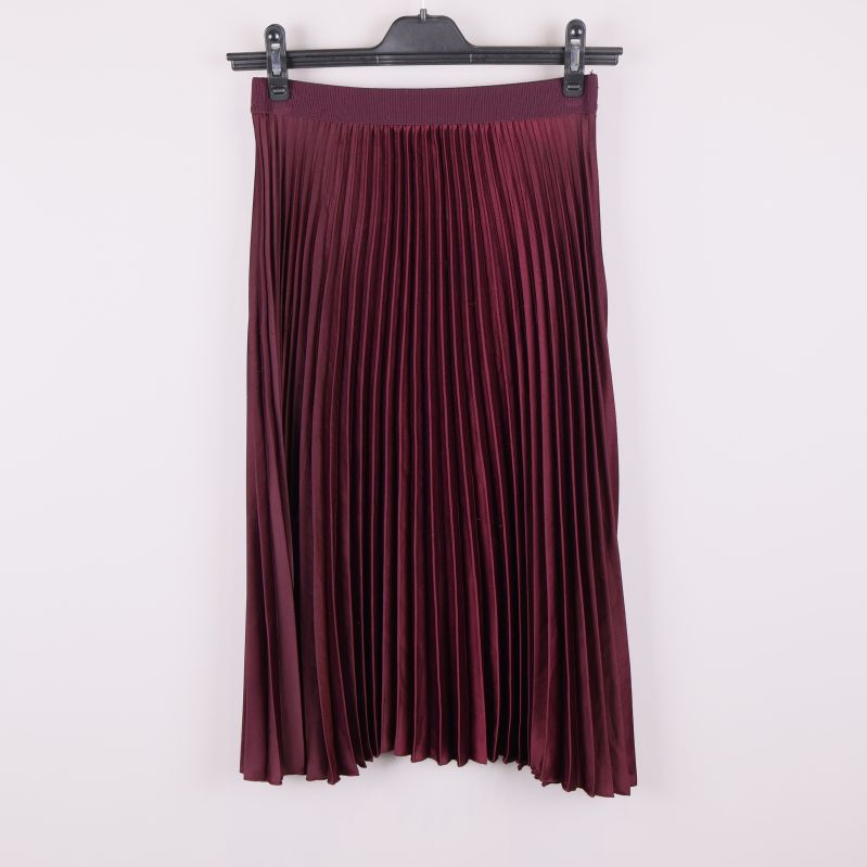 Vinröd plisserad kjol på galge mot vit bakgrund