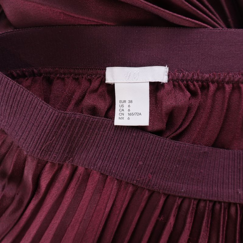 Storleksetikett H&M, visar elastisk midja på vinröd kjol