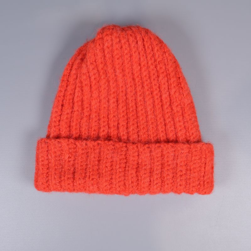 Orange ribbad stickad mössa sedd framifrån på grå bakgrund