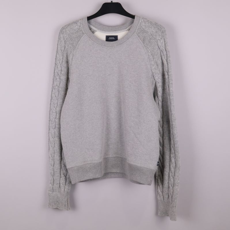 Grå stickad tröja på galge mot ljus bakgrund