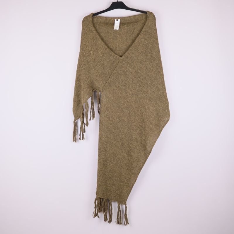 Stickad brun poncho med fransar på galge mot ljus bakgrund