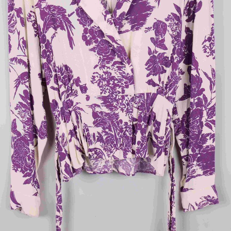 Nedre del av omlottblus med knytdetalj och lila blommönster