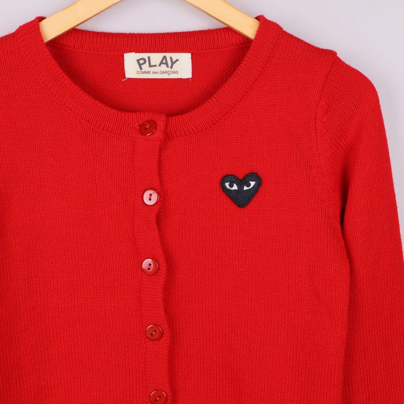 Närbild på röd kofta med svart hjärtapplikation och knappar