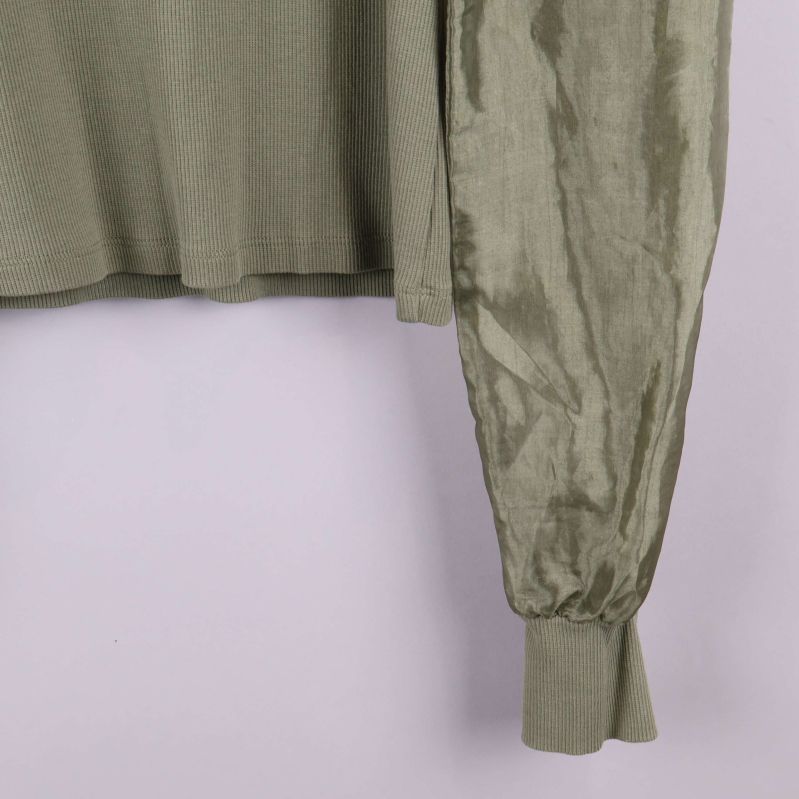 Närbild på ärmslut i glansigt tyg och mudd på olivgrön tröja