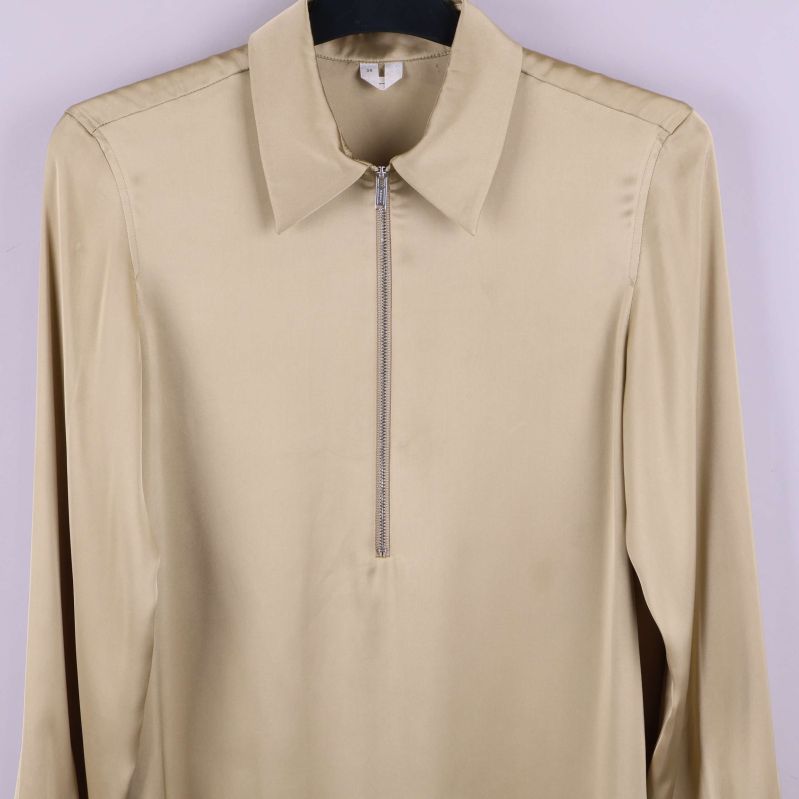 Närbild framtill på beige blus med dragkedja och krage