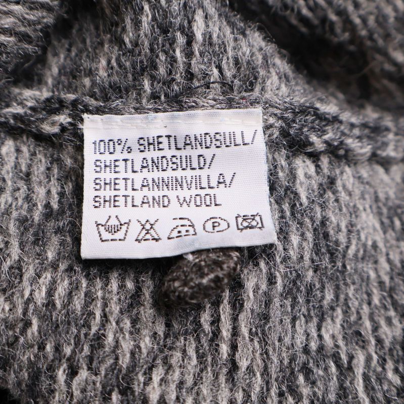 Materialetikett som visar 100% shetlandsull på flera språk