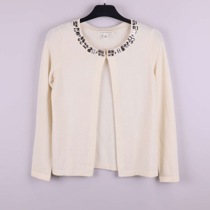 Krämpfärgad kofta hänger på galge med dekor runt halsen