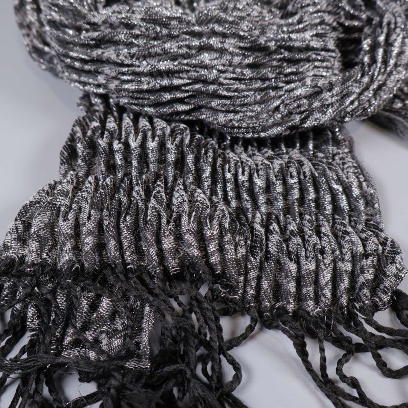 Närbild på stickad struktur och fransdetaljer i svart och silvergrått