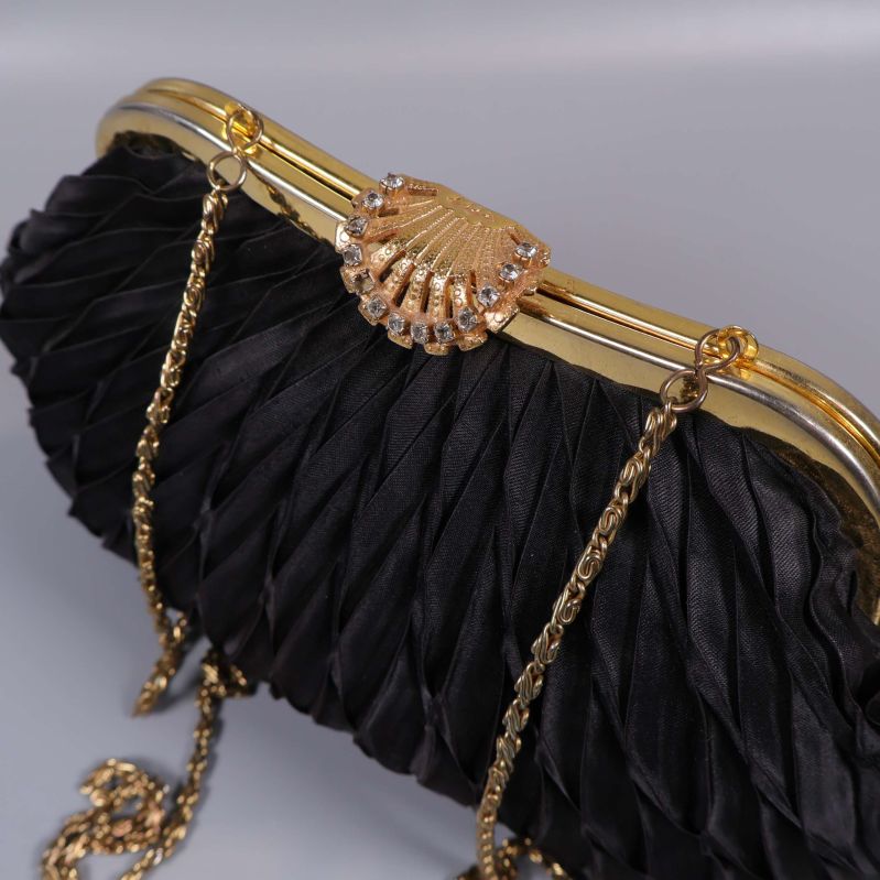 Närbild på guldigt snäckspänne och kedjerem på svart väska