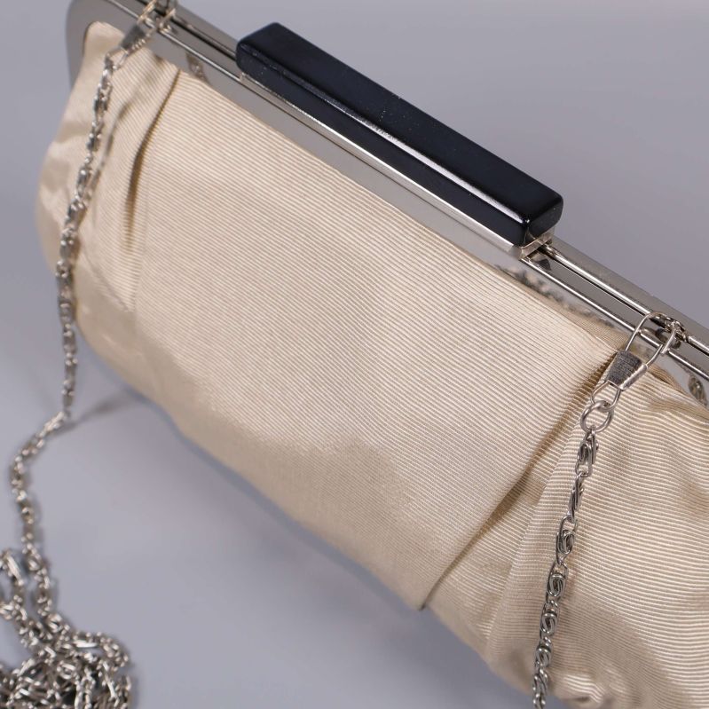 Närbild på väskans silverram, beige tyg och kedja