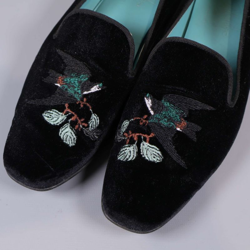 Närbild på broderad fågel och bladmönster på tån