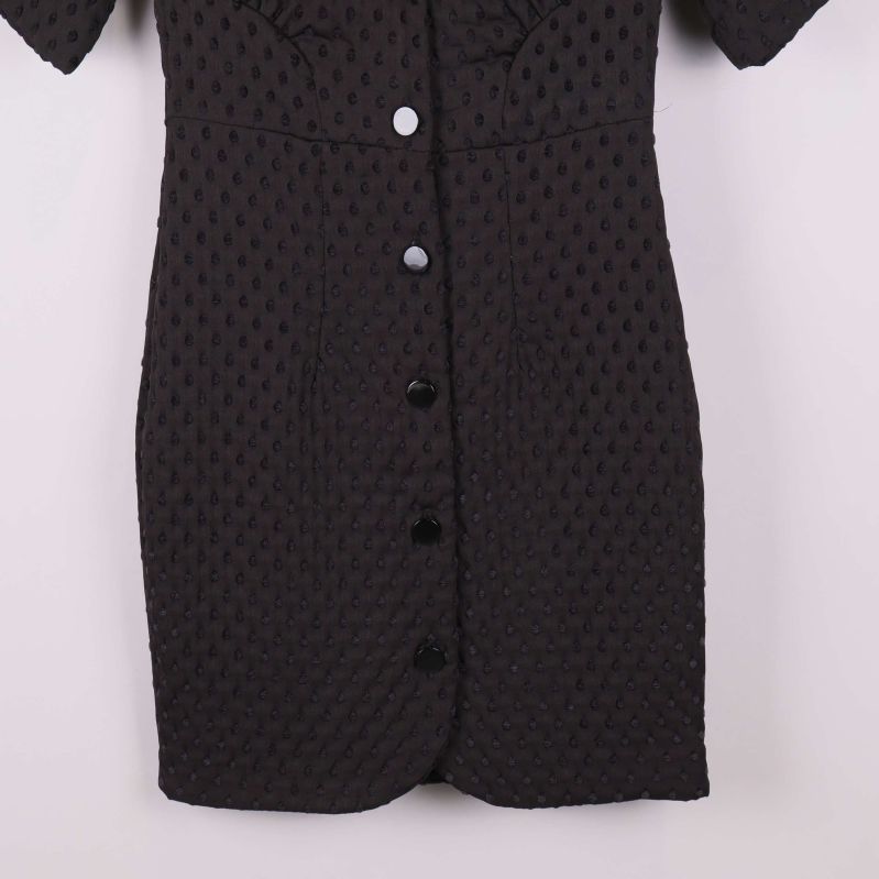 Närbild på nederdelen av svart klänning med knappslå