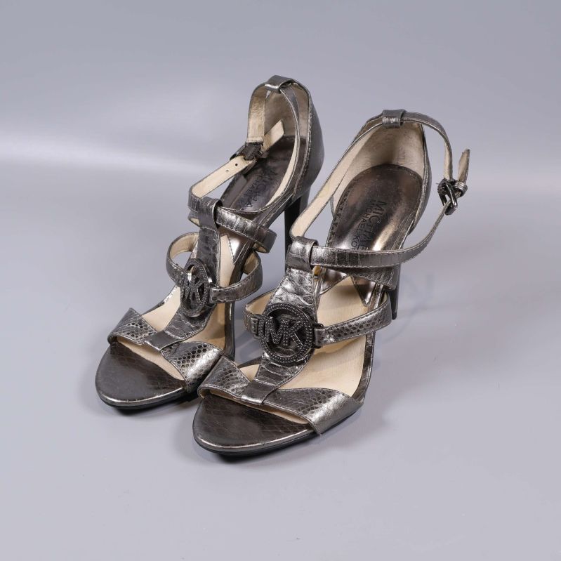 Ett par högklackade sandaler med remmar och MK-emblem framtill