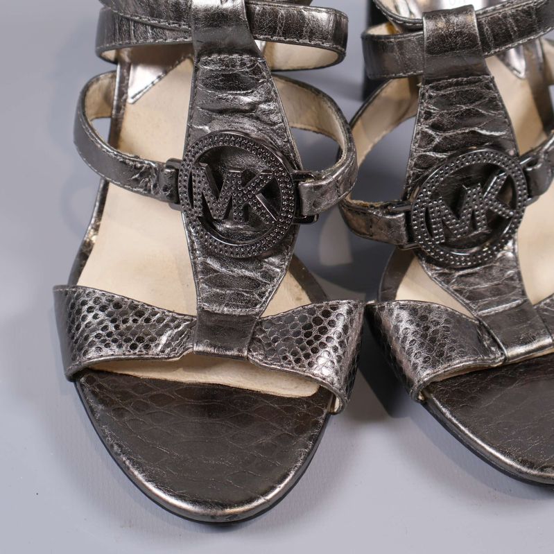 Närbild på sandaler med MK-emblem och strukturmönster