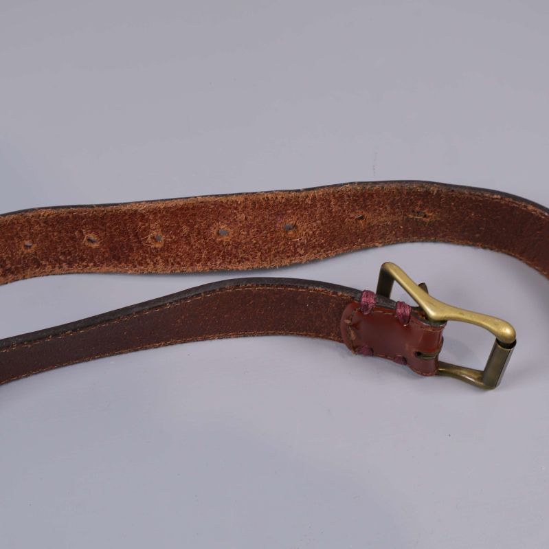 Brunt läderbälte öppnat med mässingsspänne mot vit bakgrund