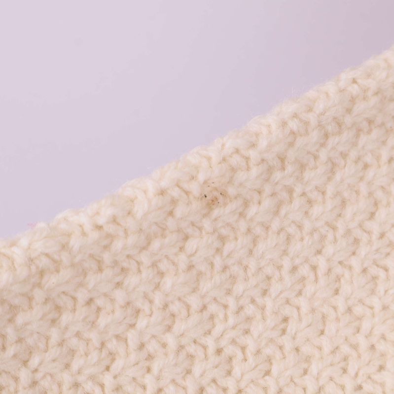 Närbild på axelparti med stickad struktur och liten fläck