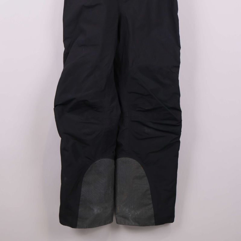 Nederdel av benen på svart hängselbyxa med grå förstärkning