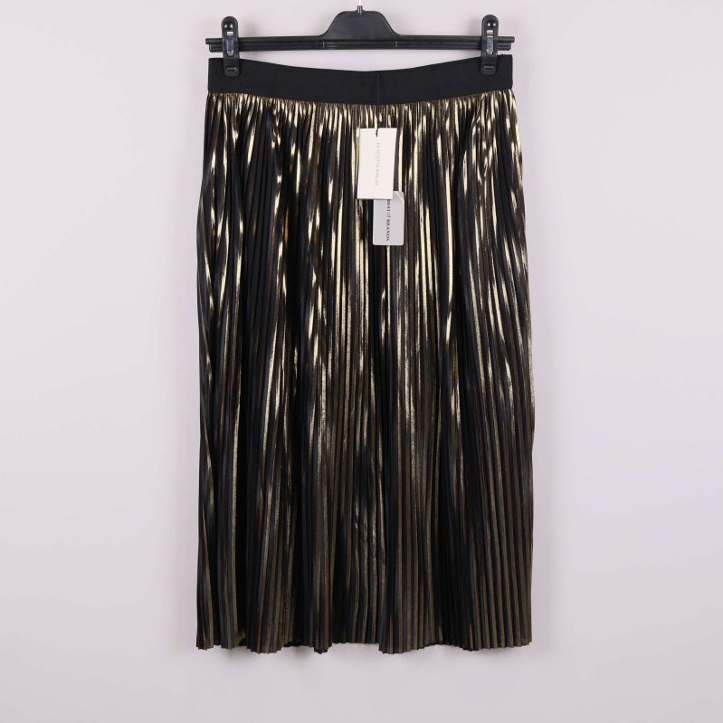 Plisserad kjol i svart och guld hängandes på galge mot ljus bakgrund