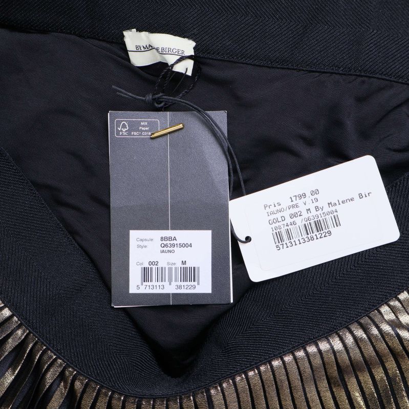 Närbild på etiketter och storlekslapp inuti svart och guld plisserad kjol