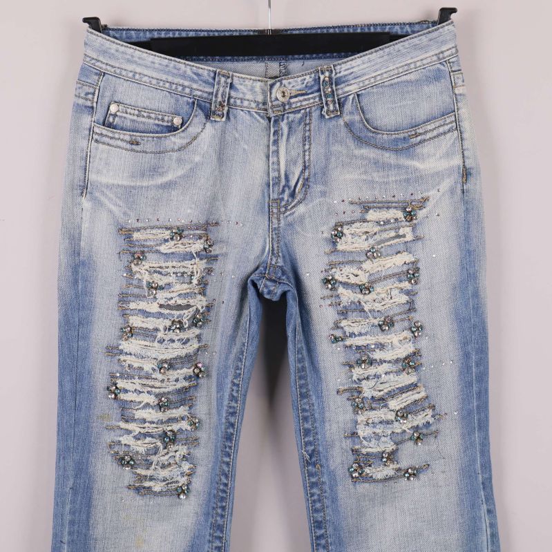 Närbild av slitningar och paljettdetaljer framtill på jeans