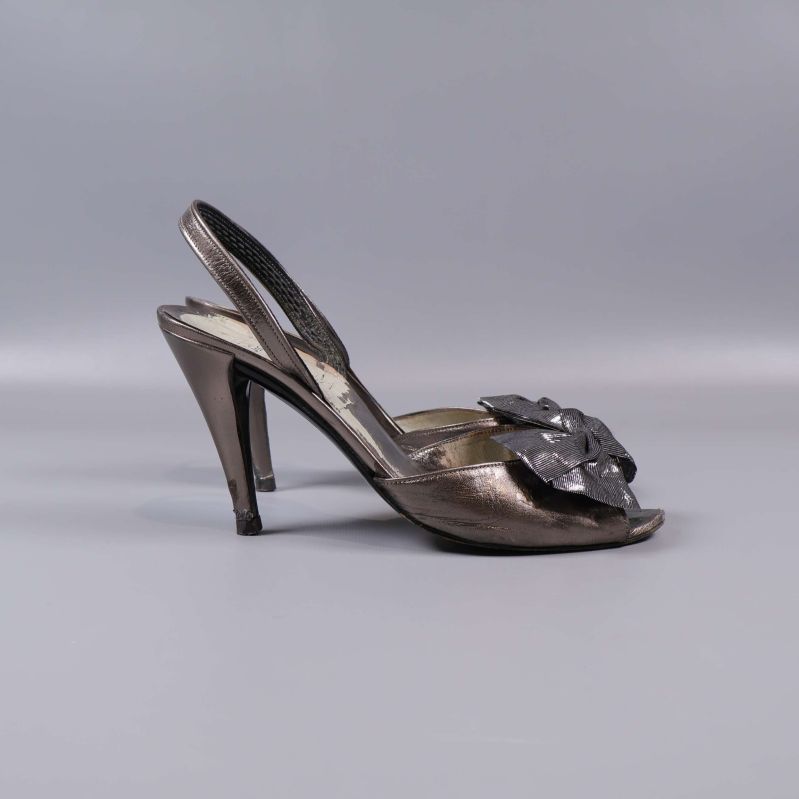 Sida av klackskor med metallisk yta och rosett