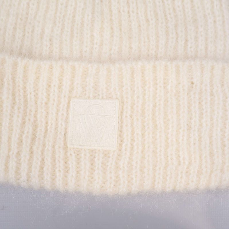 Närbild på logotypmärke på vit stickad mössa