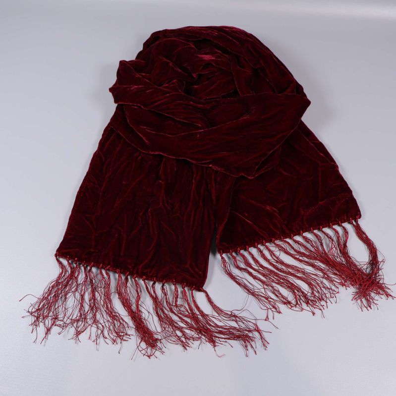 Vinröd halsduk med fransar liggande vikt på bord