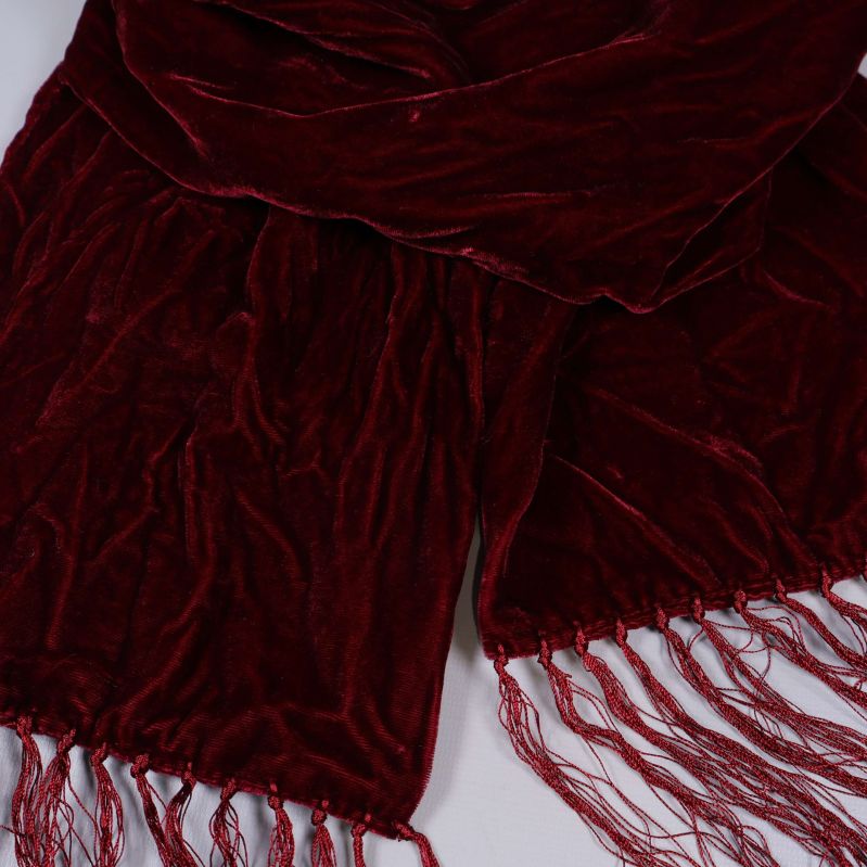 Närbild på vinröd halsduk med fransar och glansig struktur