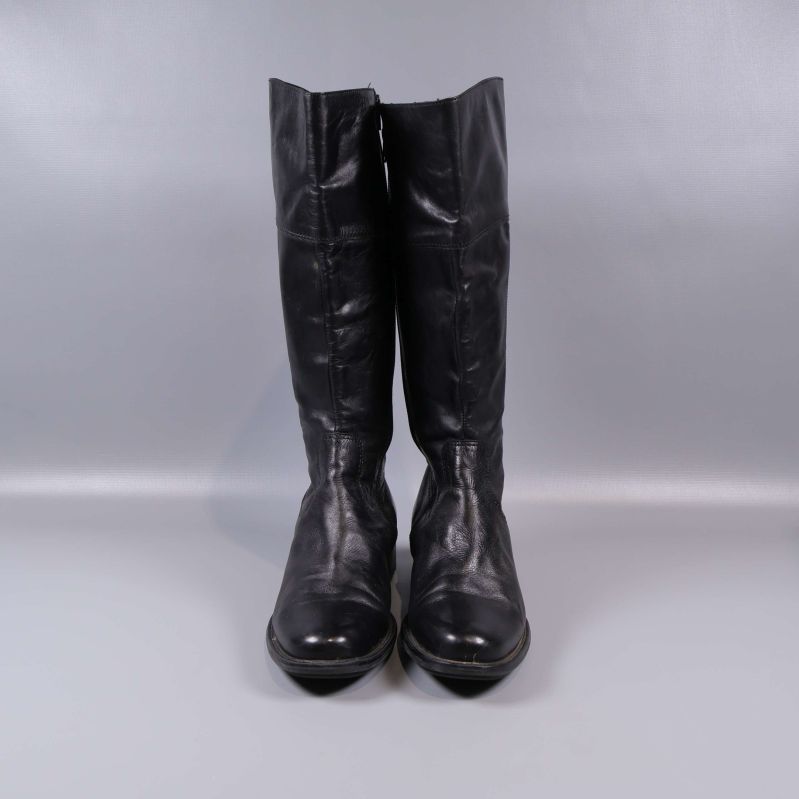 Framifrån av höga svarta stövlar på grå bakgrund