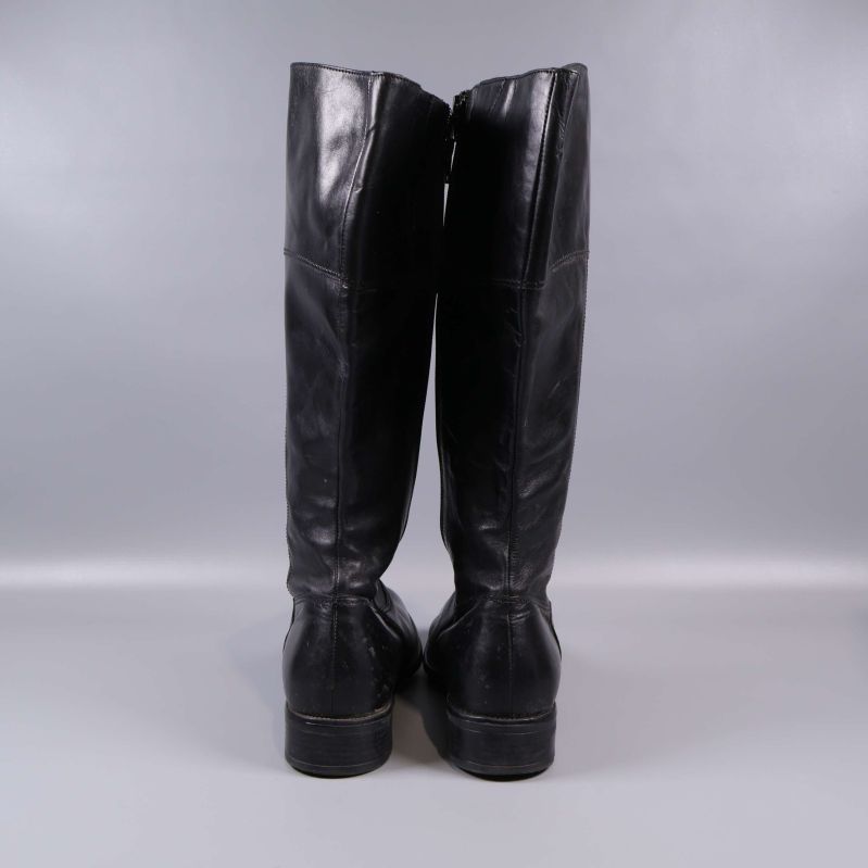 Baksida på höga svarta stövlar mot grå bakgrund