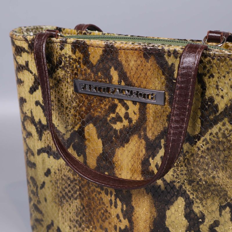 Närbild på väska med ormmönstrad yta och metallogo