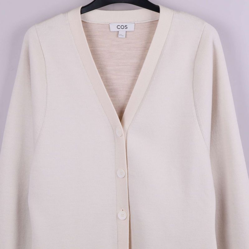 Närbild på V-ringning och knäppning på beige cardigan