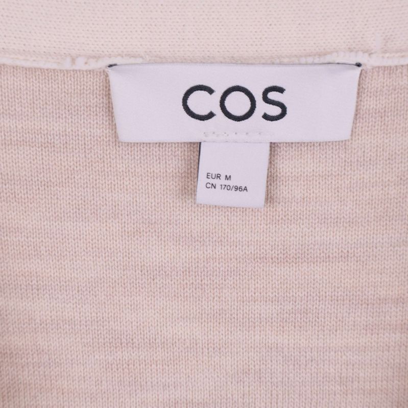 Närbild på COS-logotyp och storleksetikett i beige cardigan
