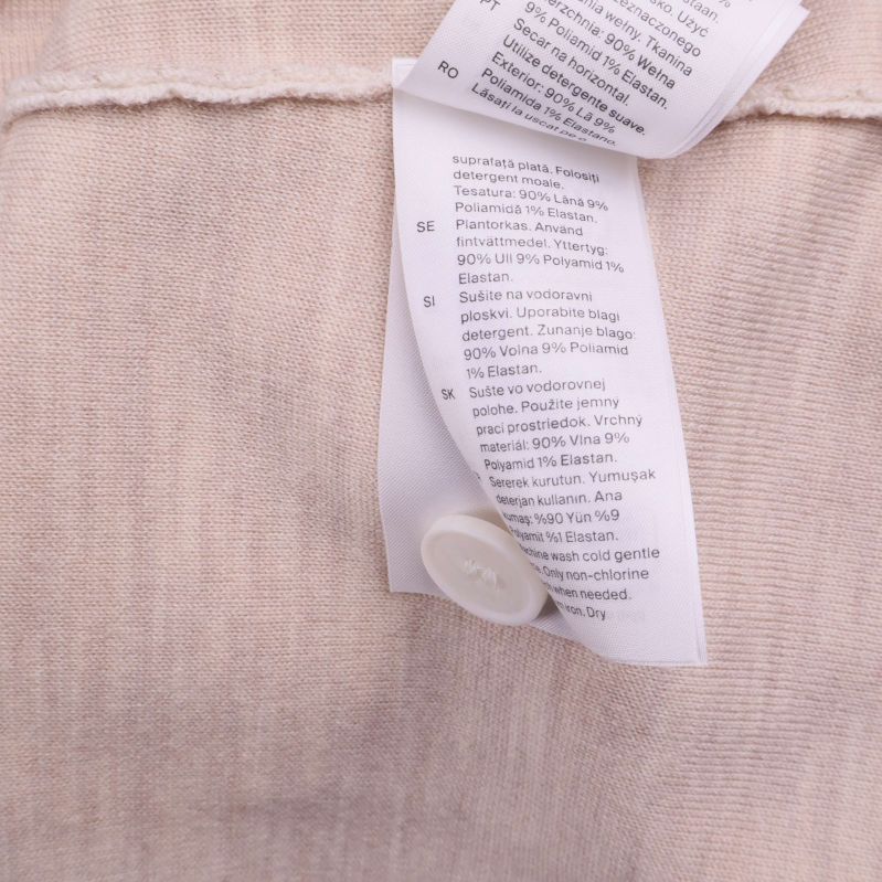 Närbild på materialetikett i beige cardigan