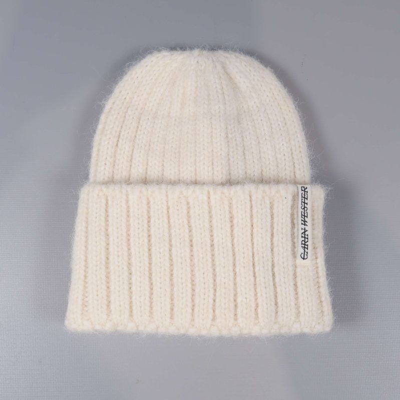 Krämvit ribbstickad mössa sedd framifrån med etikett