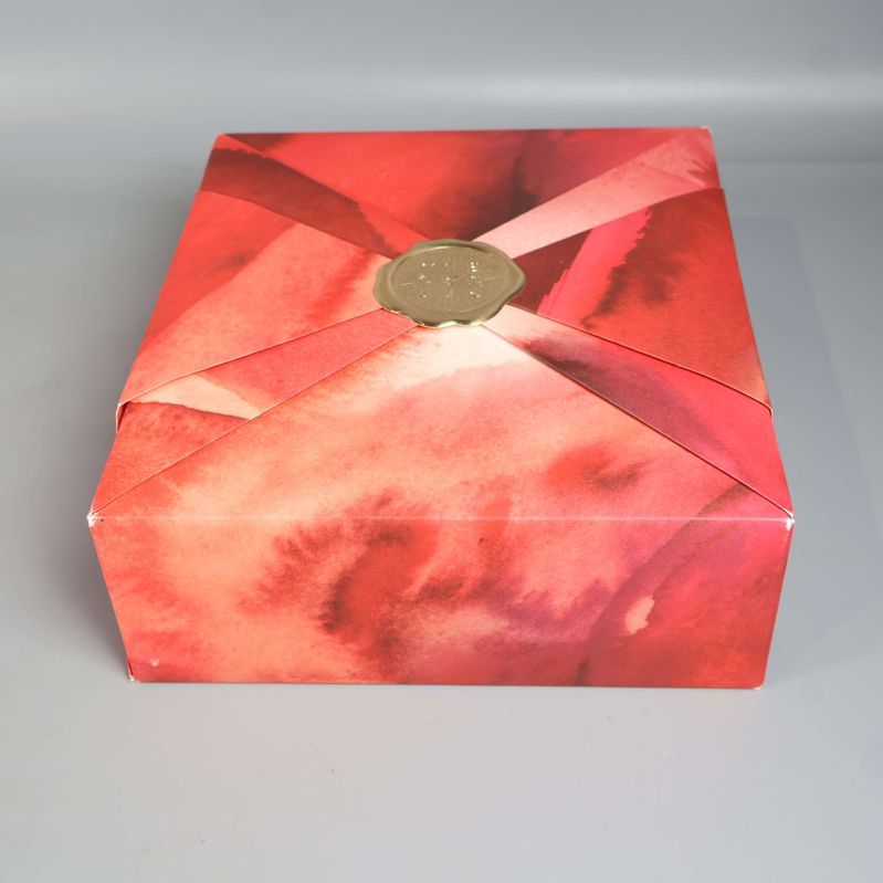 Toppvy över presentbox med rödrosa akvarellmönster och gulddetalj