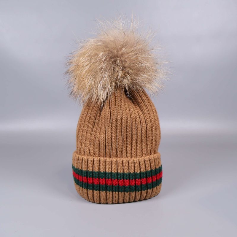 Beige stickad mössa med tofs stående på plan yta