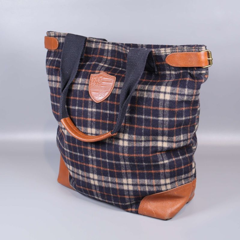 Framsida av rutig tygväska med bruna läderdetaljer och handtag