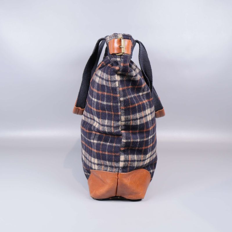 Sidan av rutig tygväska med brunt läder i botten