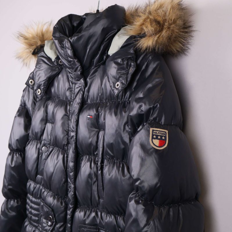 Närbild på axel med logo och fuskpälsdetalj vid huva