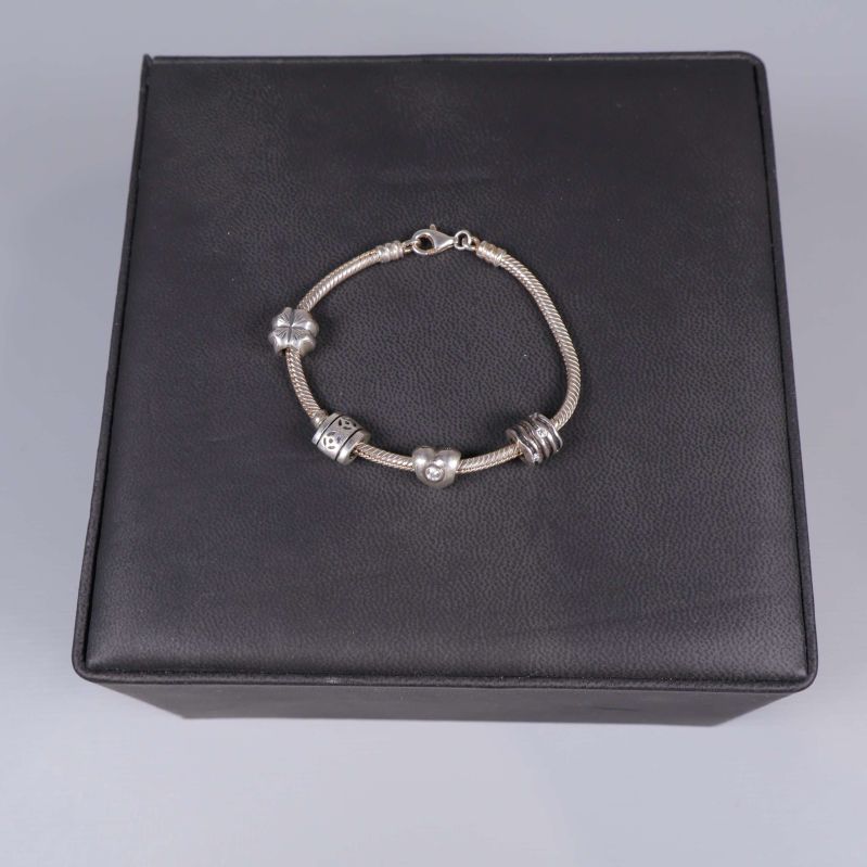 Silverfärgad armbandslänk med berlocker på svart underlag