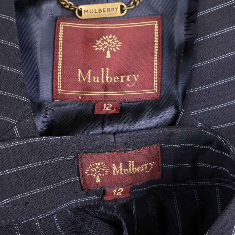 Närbild på Mulberry-logga i röd märkning på blazer och byxor