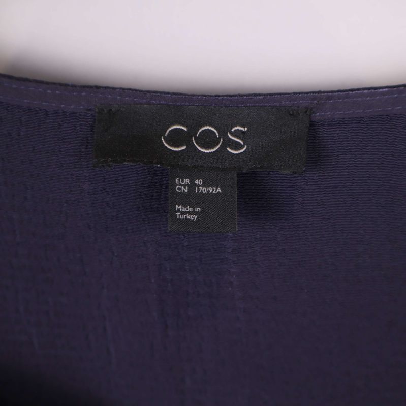 Närbild på COS-logotyp i nacklinning på klänning