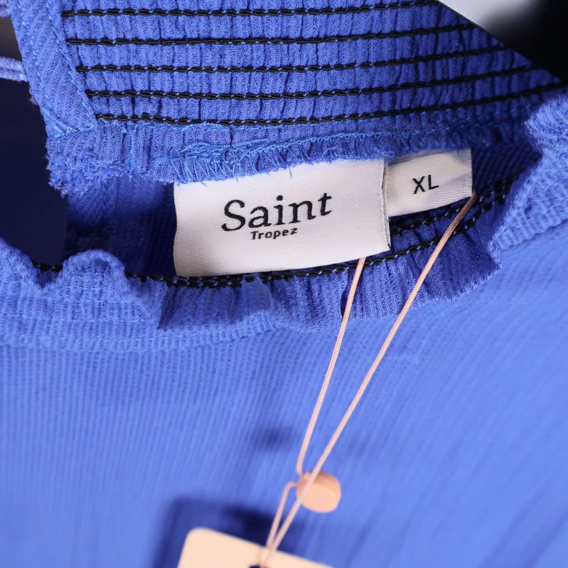 Närbild på rund hals med volang och etikett Saint Tropez XL