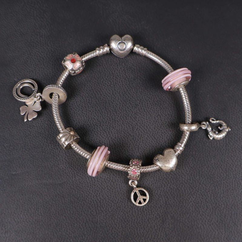 Närbild på armband med silver- och rosa berlocker liggande på svart underlag