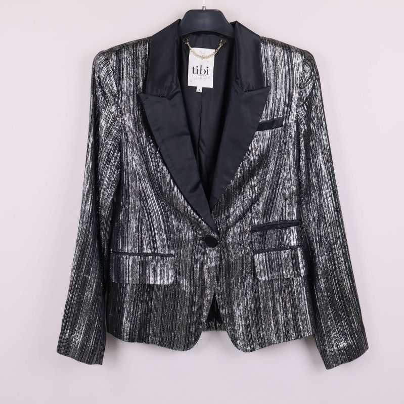 Kavaj med glittrande yta och svarta detaljer på galge