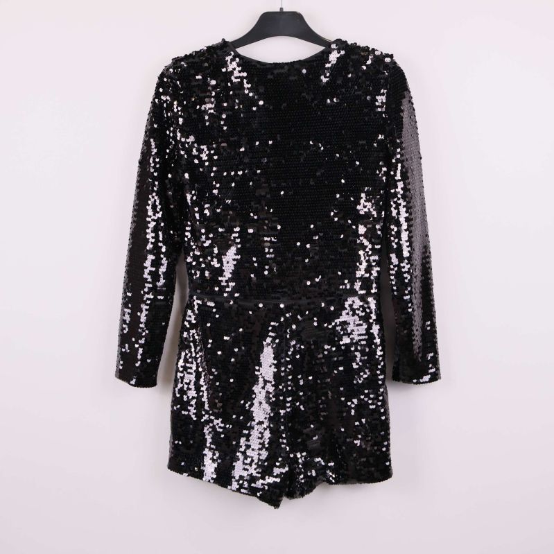 Baksidan av svart paljettjumpsuit på galge mot ljus bakgrund