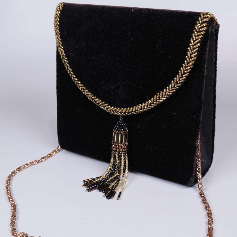 Närbild på svart väska med dekorativ guldkedja och tofs