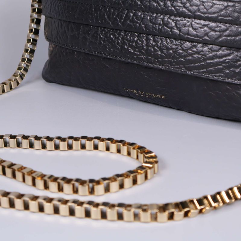 Närbild på kedjerem och nederkant av svart väska