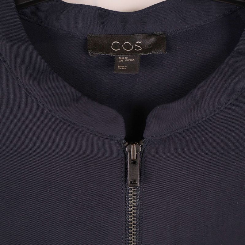 Närbild på halsringning och dragkedja samt COS-märke